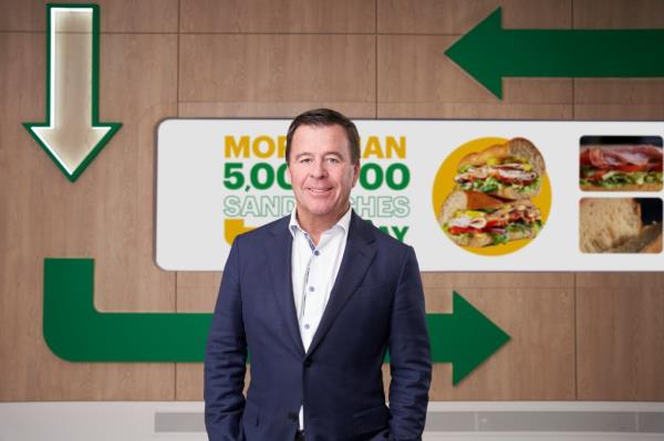 John Chidsey wearing a suit standing in front of a Subway sign.